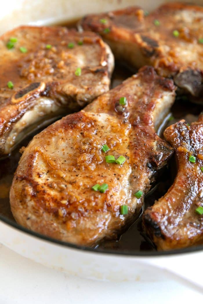 White skillet filled with seared bone-in pork chops simmered in a sweet and sticky honey garlic sauce.