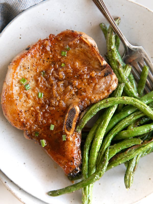 Close up overhead image of a white serving plate filled with one bone-in honey garlic pork chop and a side of green beans.