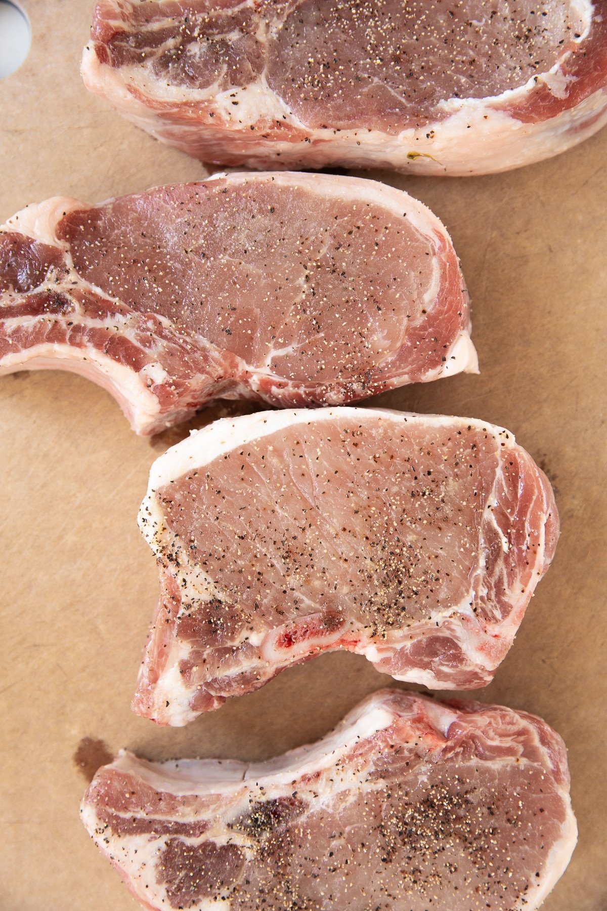 Four bone-in pork chops on a large cutting board.