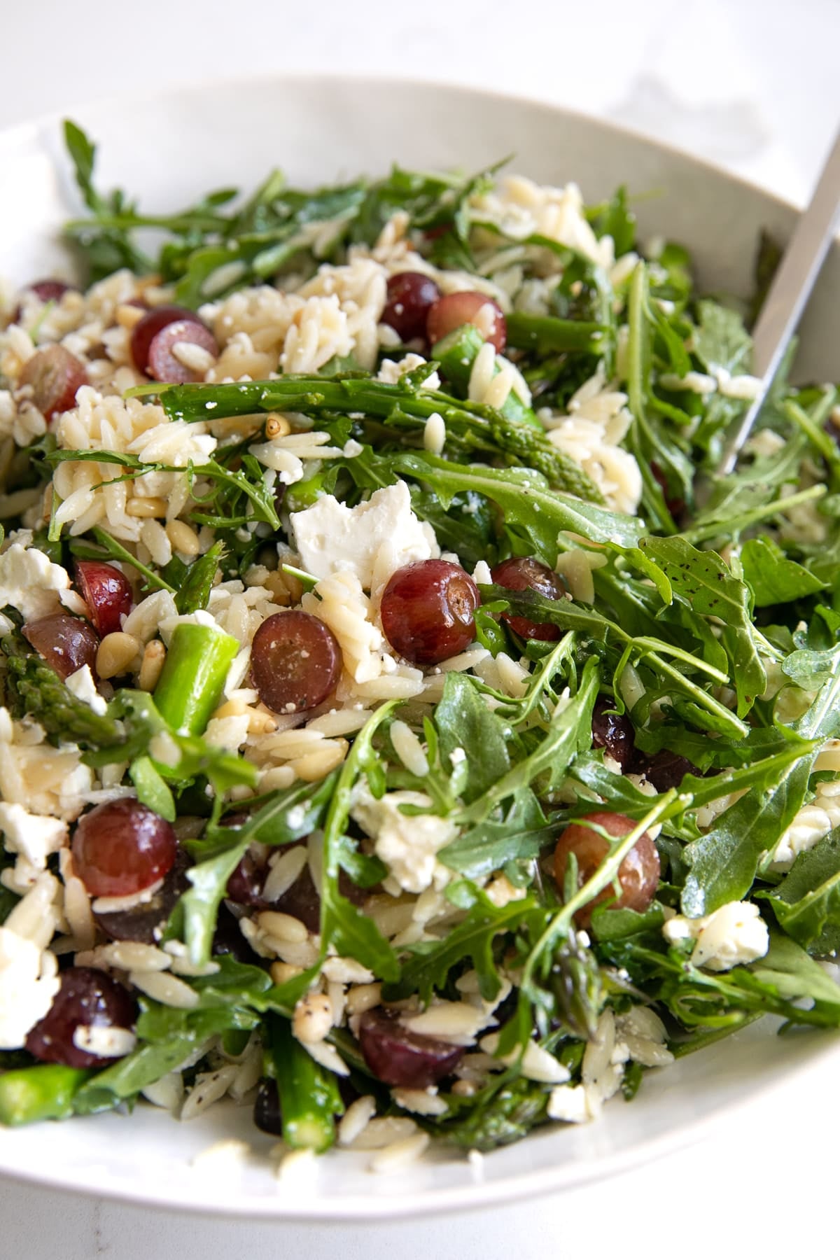 Image of a large salad bowl filled with orzo and arugula salad filled with feta cheese and grapes.