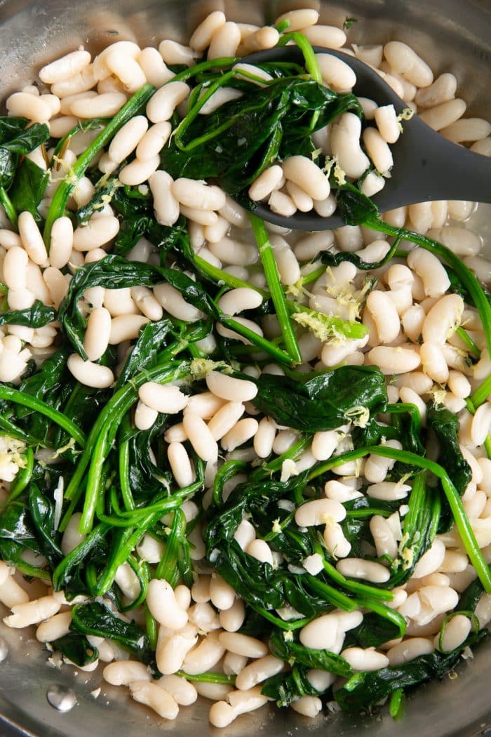 Overhead image of a large stainless steel skillet filled with cooked cannellini beans and spinach in a savory lemon and garlic sauce.