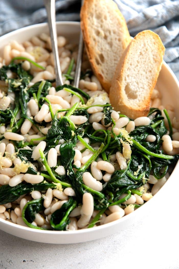 White bowl filled with cooked cannellini beans and spinach in a savory lemon and garlic sauce.