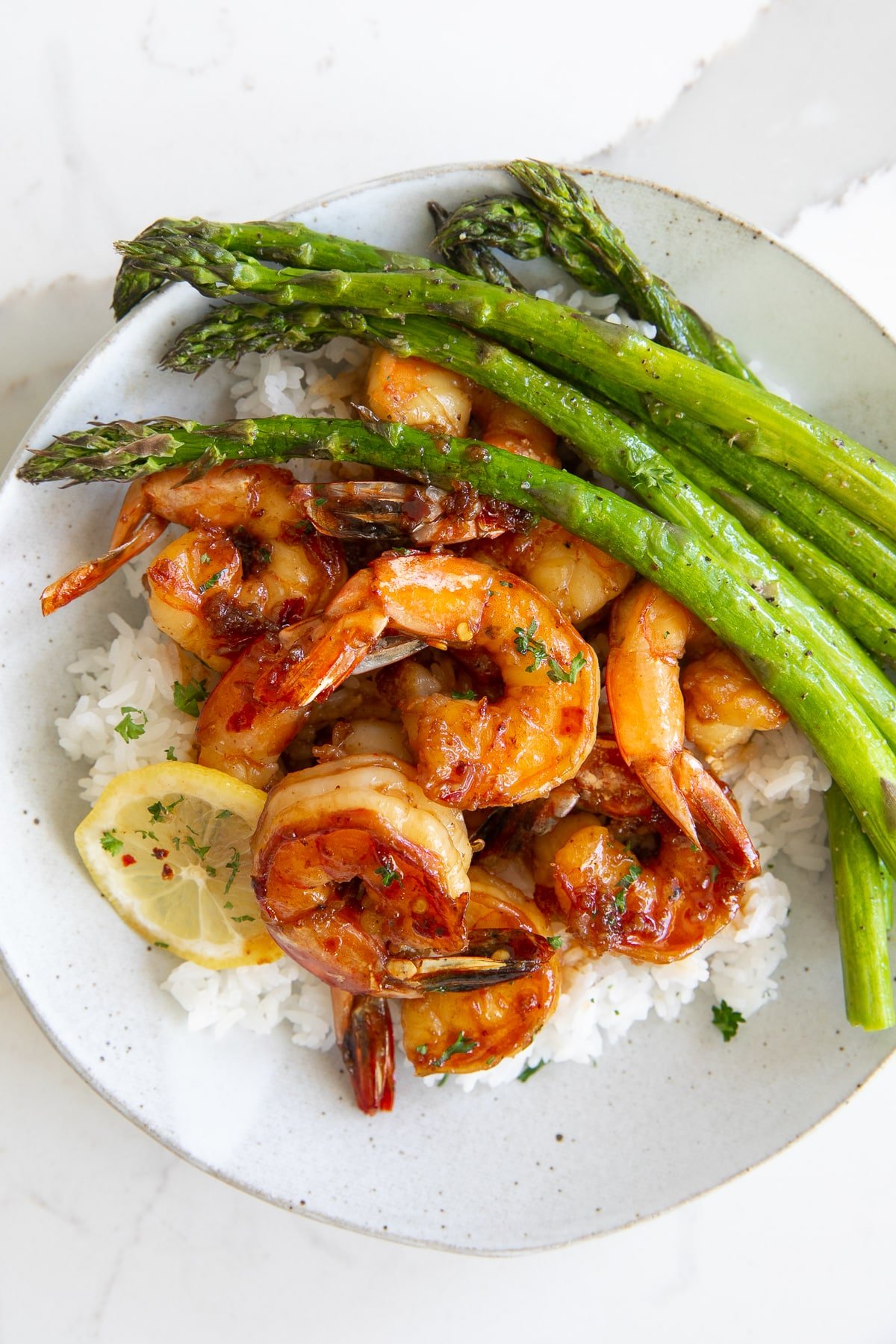 Overhead image of a white plate filled with white rice and asparagus with sweet and tangy shrimp in a honey garlic sauce.
