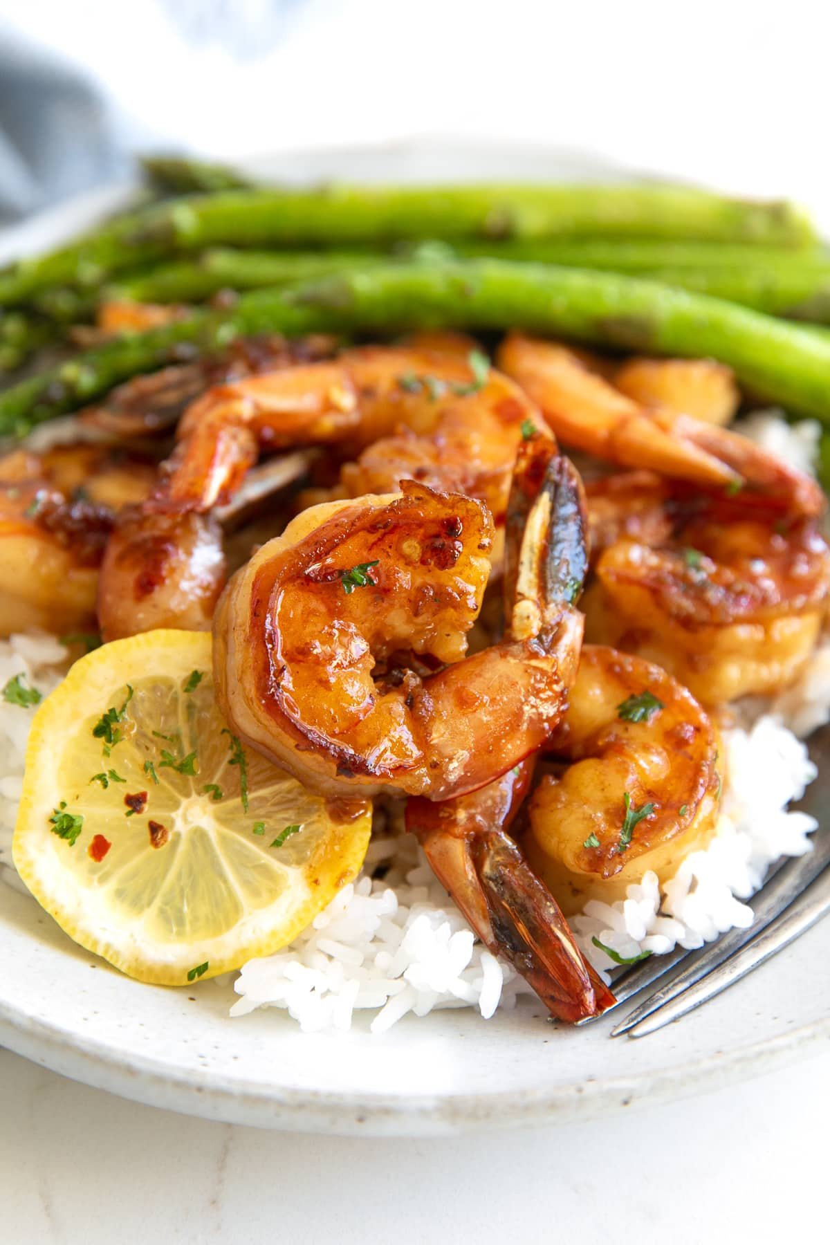 Honey garlic shrimp served with lemon slices set on top of cooked white rice and served with a side of cooked asparagus.