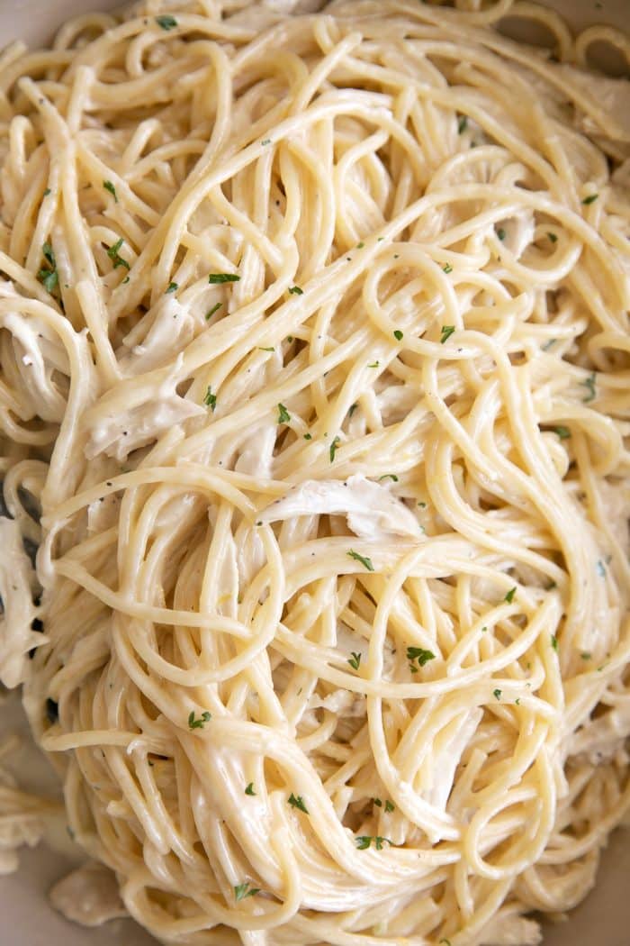 Close up overhead image of spaghetti noodles and shredded chicken mixed in a homemade creamy lemon garlic sauce.