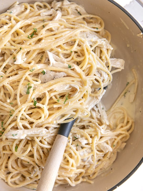 Large white Dutch oven filled with cooked spaghetti noodles and cooked shredded chicken in a rich and creamy lemon garlic sauce.