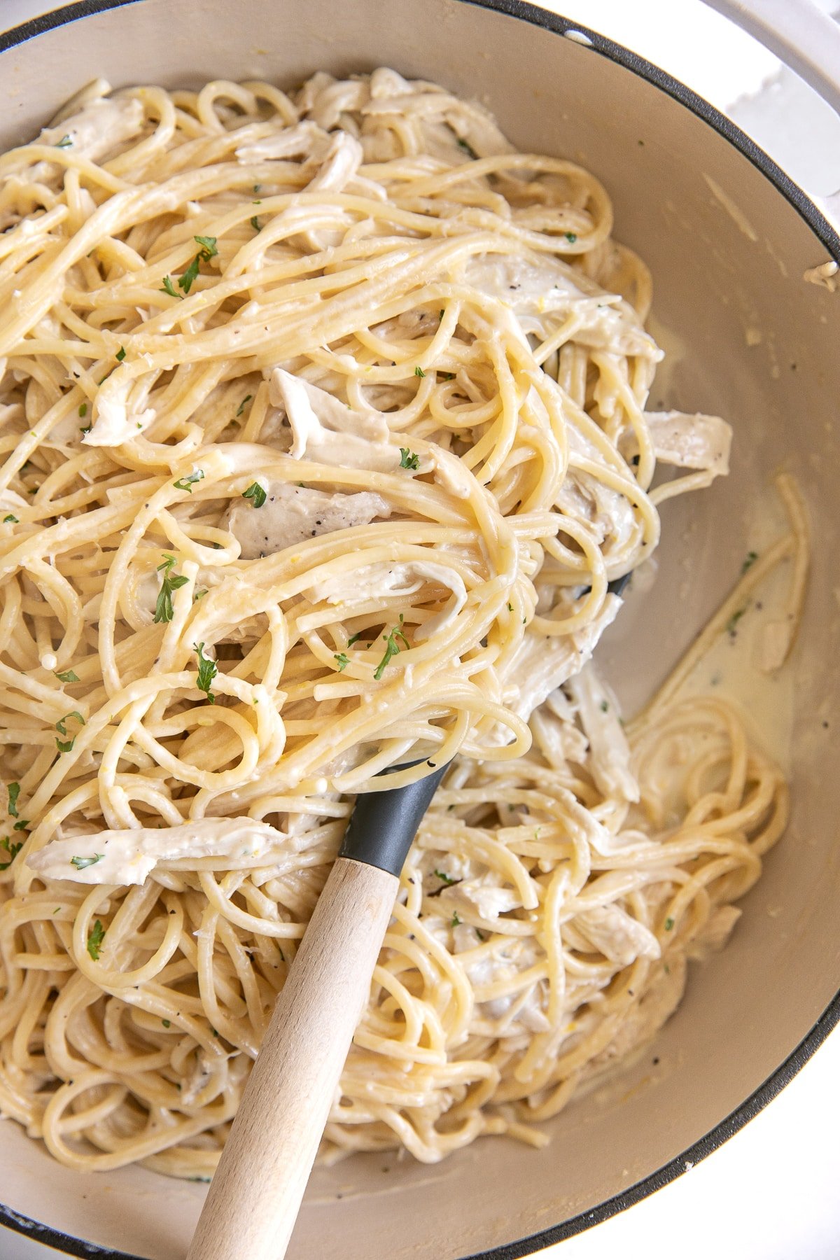 Large white Dutch oven filled with cooked spaghetti noodles and cooked shredded chicken in a rich and creamy lemon garlic sauce.