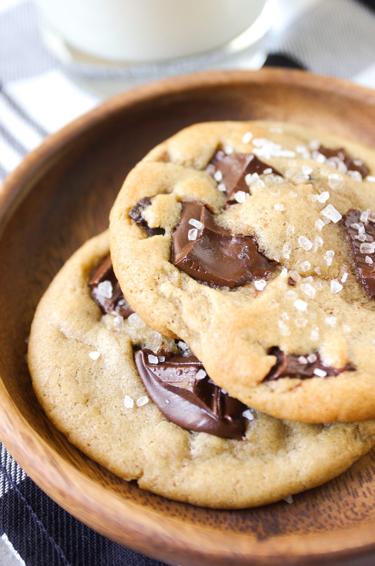 two large chocolate chunk cookies close up with melted chocolate and salt crystals on top in a wooden bowl.