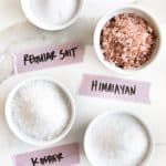 Image of the four types of salt (regular salt, Himalayan, kosher, and sea salt) each in their own white ramekin and labeled on light purple tape.