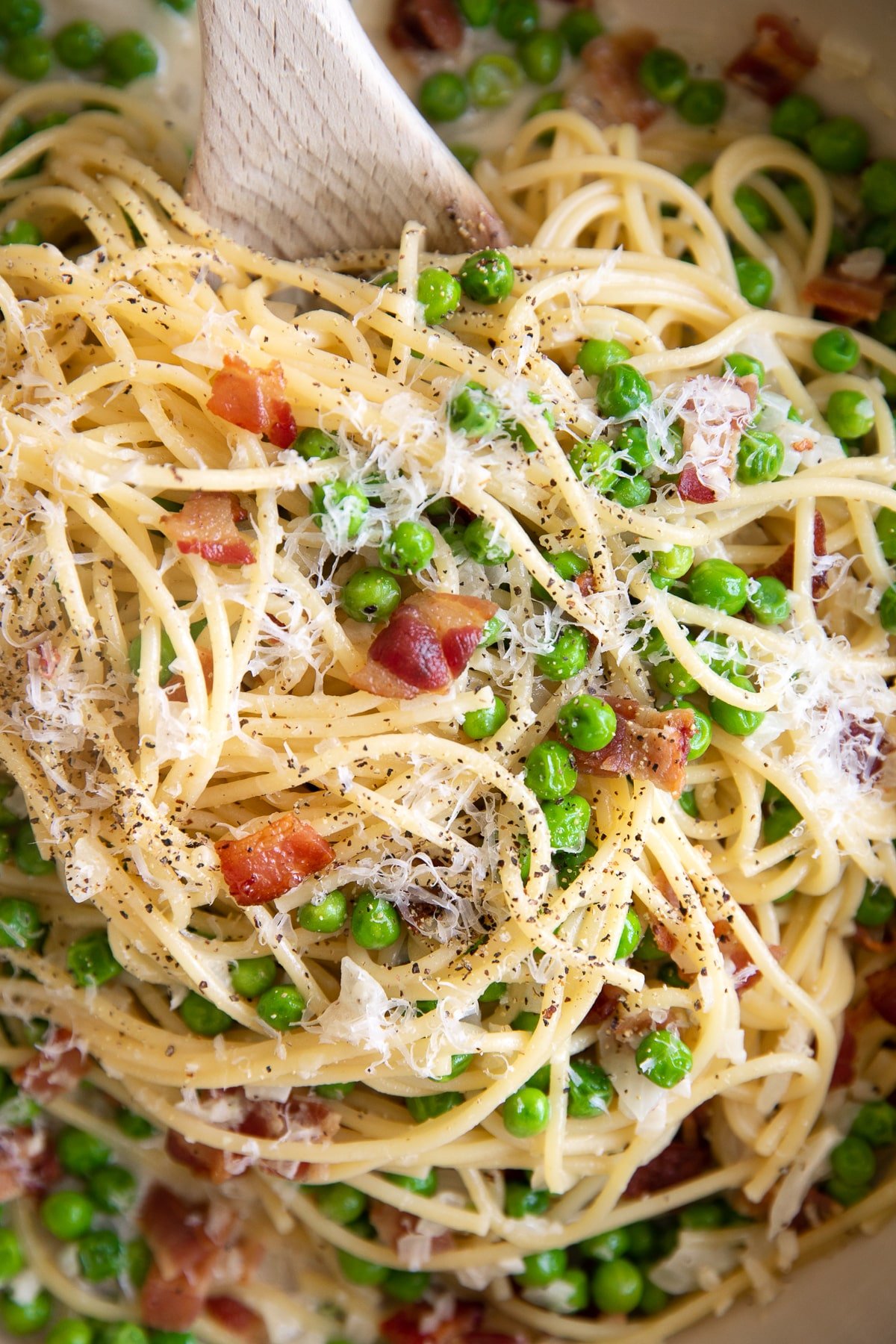 Close up image of spaghetti noodle pasta with bacon and peas in a cream sauce and garnished with fresh parmesan cheese and black pepper.