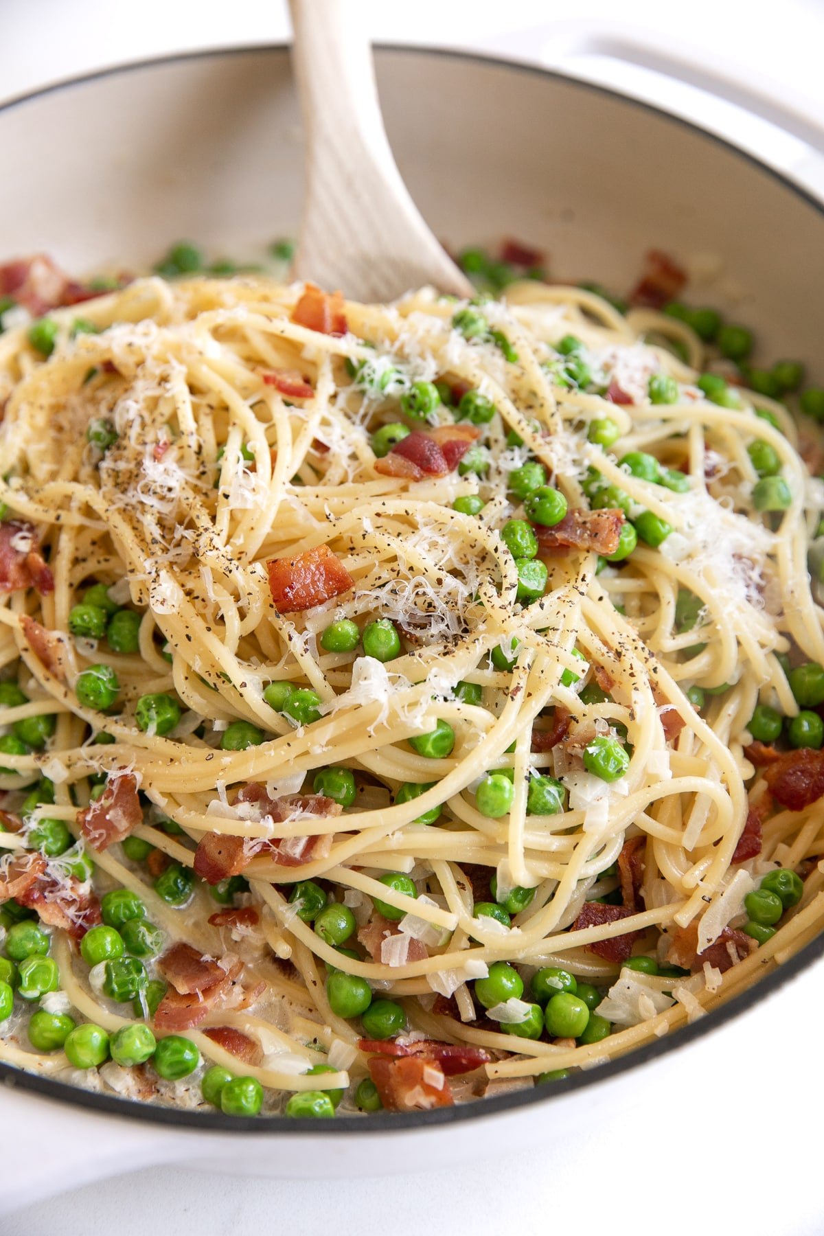 Image of spaghetti noodle pasta with bacon and peas in a cream sauce and garnished with fresh parmesan cheese and black pepper.