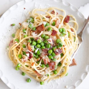 Overhead image of spaghetti noodles in a cream sauce with bacon and peas.