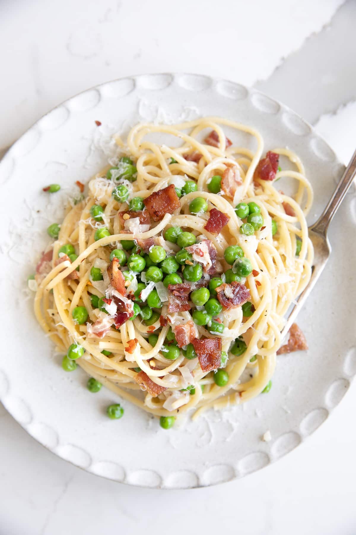 Overhead image of spaghetti noodles in a cream sauce with bacon and peas.
