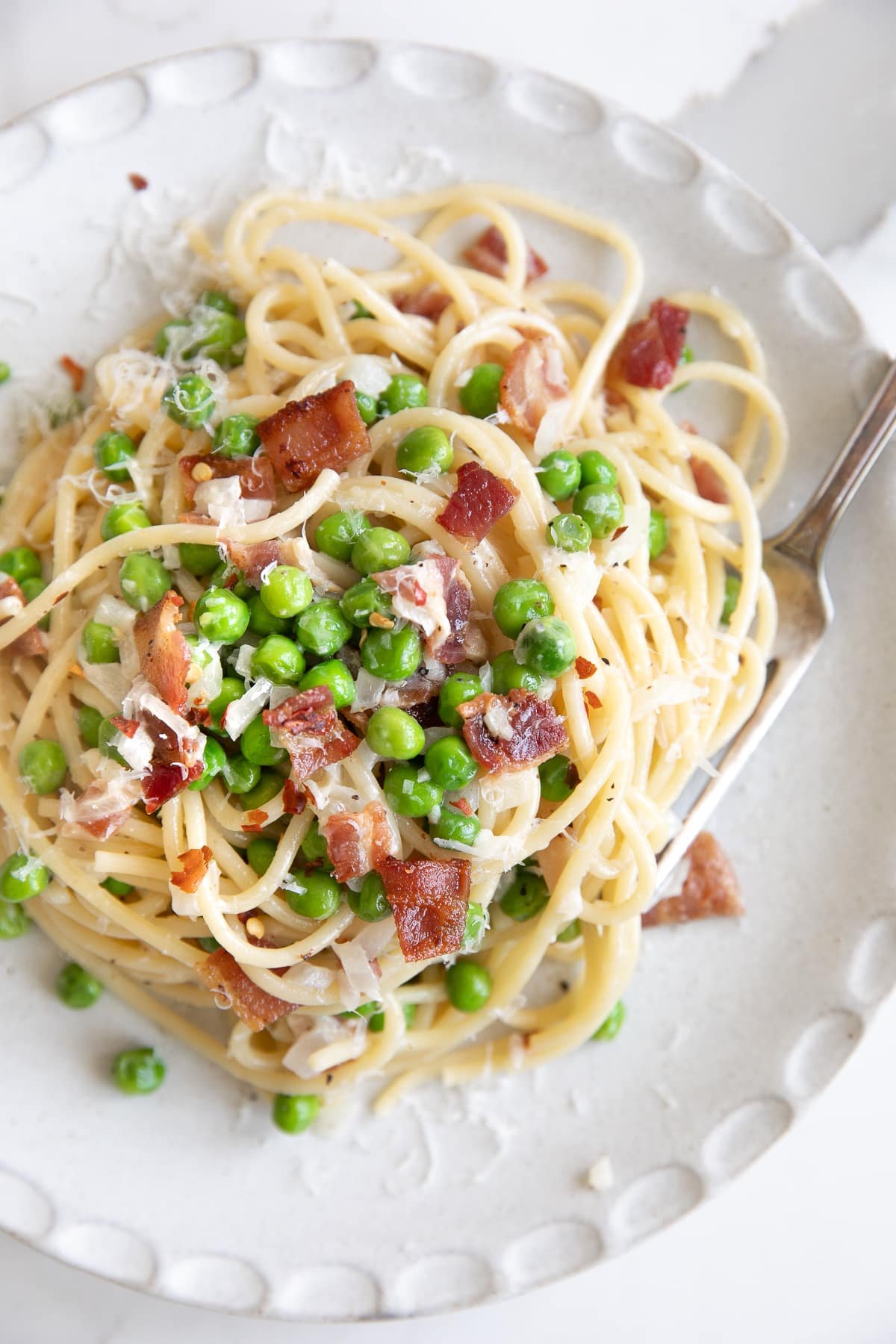 Overhead image of creamy bacon and pea pasta on a white serving plate.