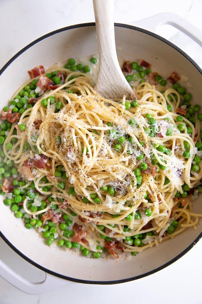 Overhead image of spaghetti noodle pasta with bacon and peas in a cream sauce and garnished with fresh parmesan cheese and black pepper.