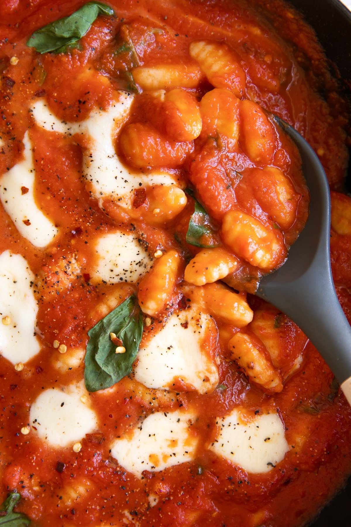 Close up image of a pan filled with gnocchi cooked in homemade tomato sauce and topped with bubby melted cheese and fresh basil.