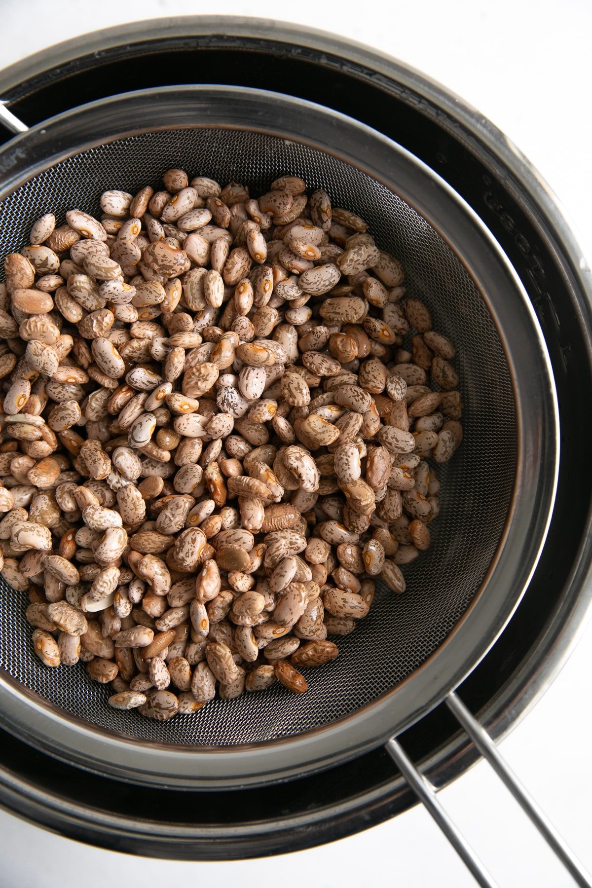 Straining dry pinto beans in a colander thats resting over a large pot.