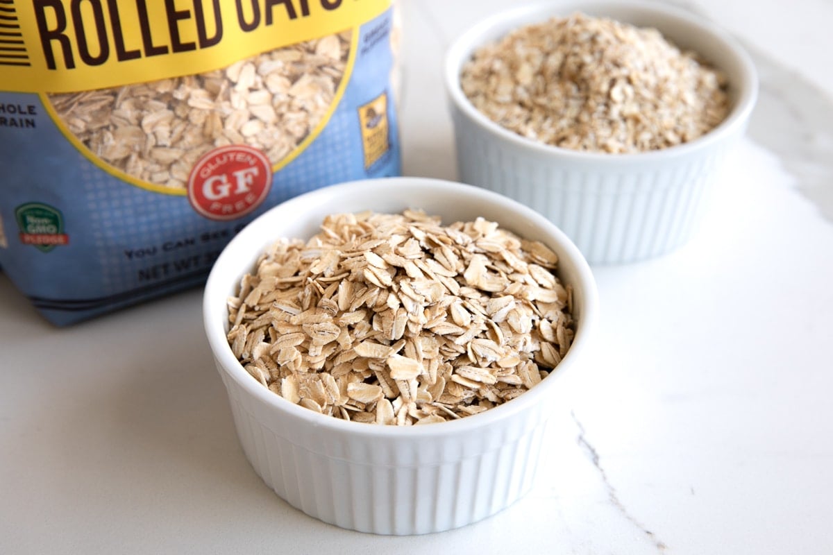 Image of two small white ramekins one is filled with rolled oats and the other is filled with quick oats.