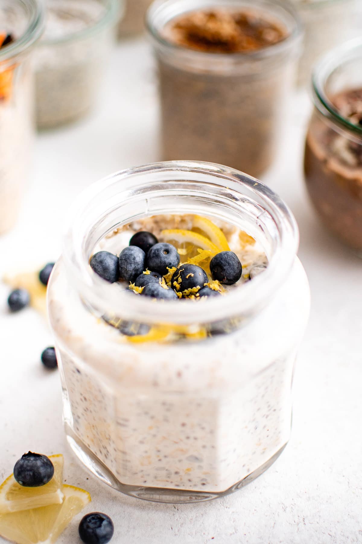 Blueberry lemon overnight oats in a faceted glass jar, topped with fresh blueberries, lemon zest, and thin lemon slices.