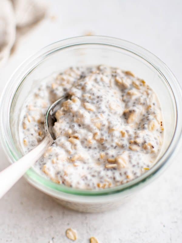 Overhead close-up of stirred overnight oats with chia seeds in a glass jar. A spoon rests inside the jar, showing the thick and creamy texture.