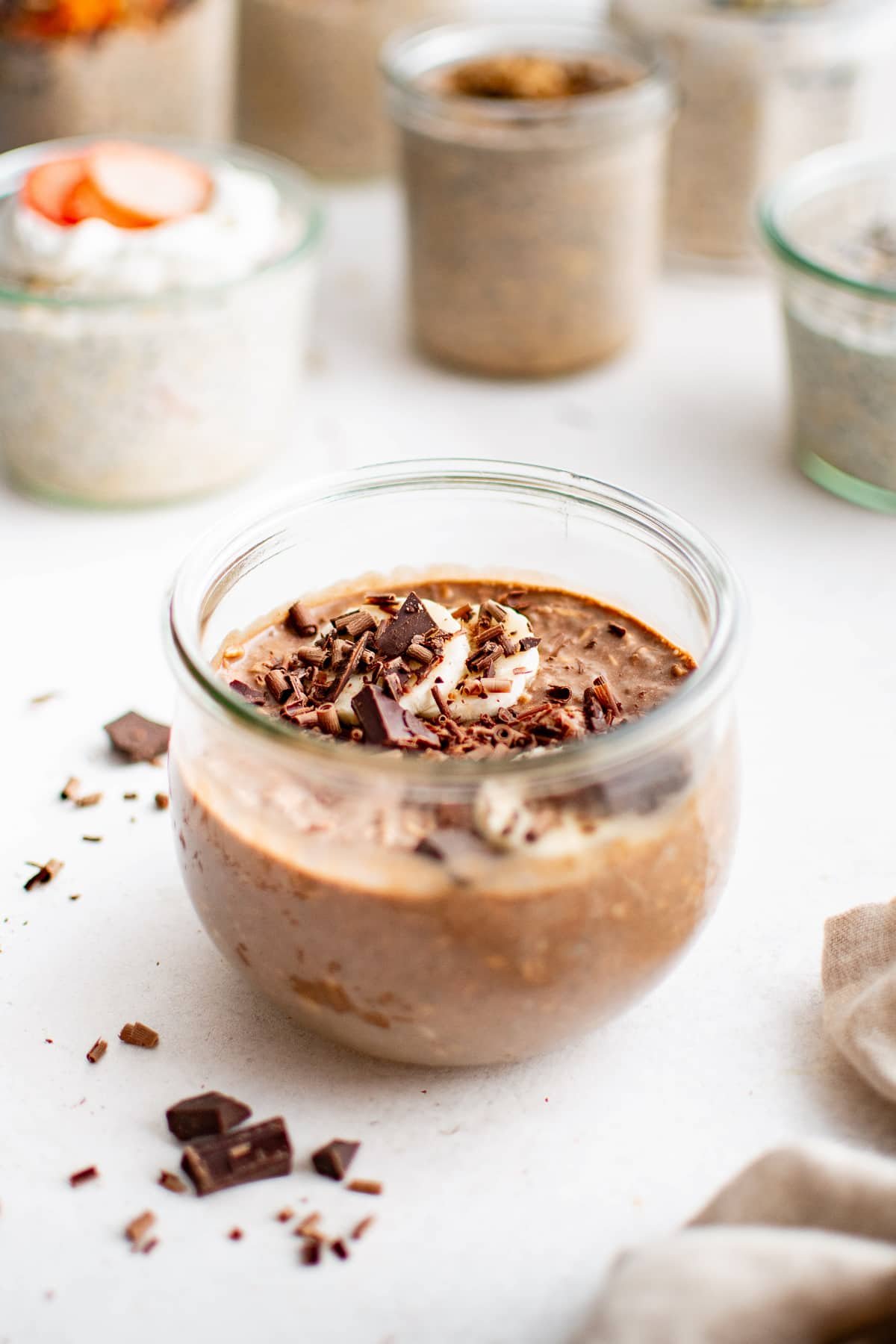 Chocolate banana overnight oats in a jar topped with sliced bananas, shaved chocolate, and chopped chocolate pieces scattered on the surface.