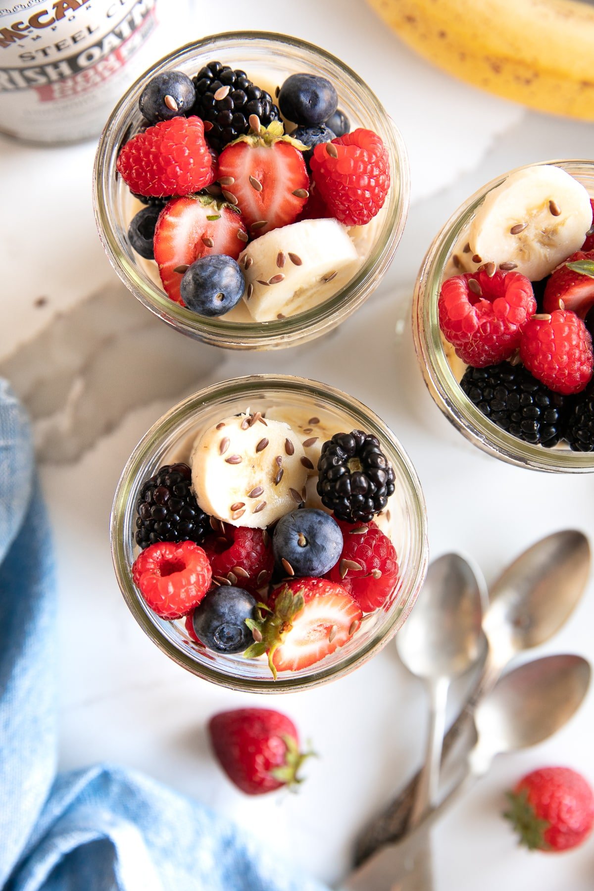 Three jars of overnight steel cut oats topped with bananas, strawberries, raspberries, and blueberries.