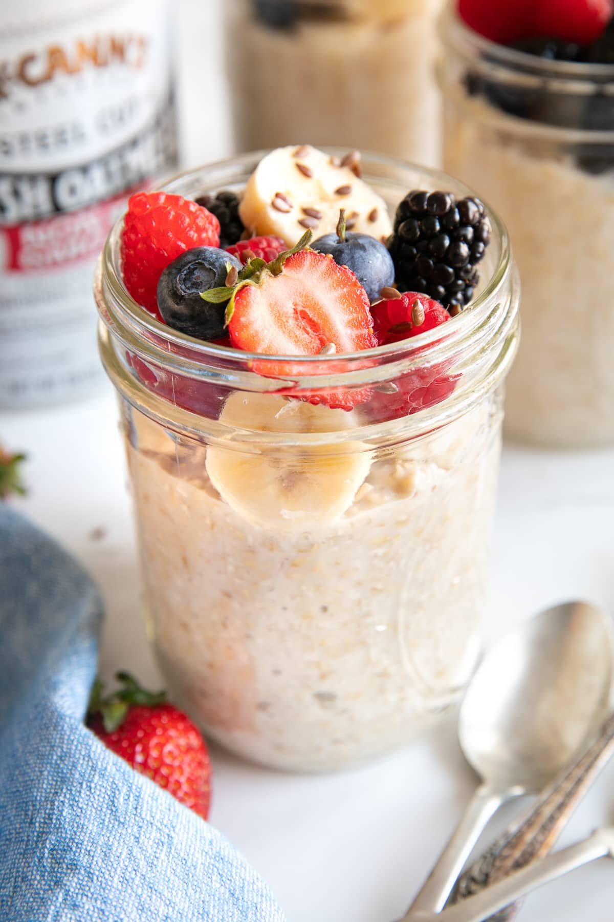 Glass mason jar filled with overnight steel cut oats and topped with sliced banana, strawberries, blueberries, raspberries, and blackberries, and sprinkled with flax seeds.
