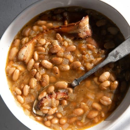 Image of cooked pinto beans with onions and bacon in a light broth.