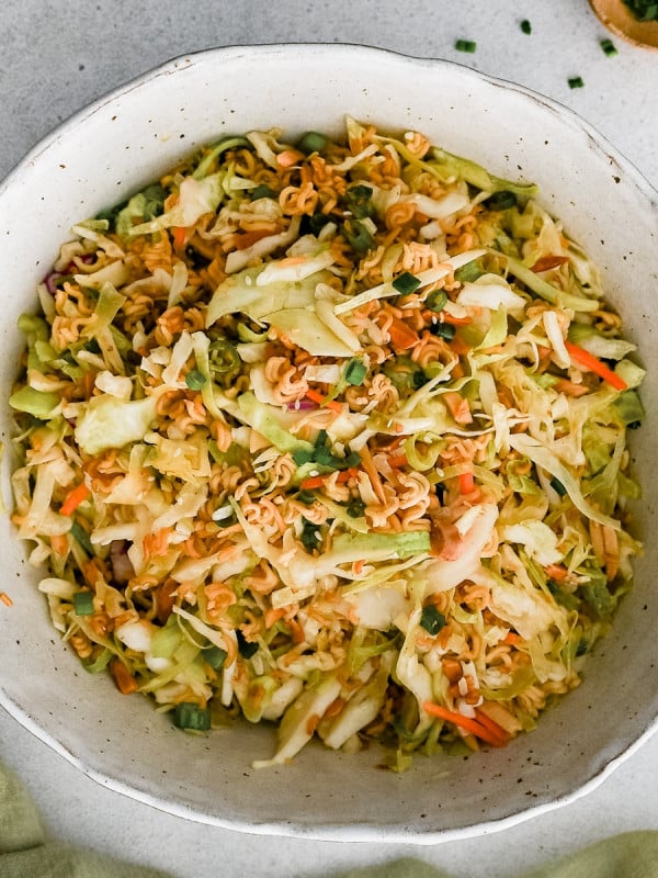 Large mixing bowl filled with a prepared ramen noodle salad consisting of toasted ramen noodles and almonds, coleslaw mix, and sliced green onions tossed in a simple sesame dressing.