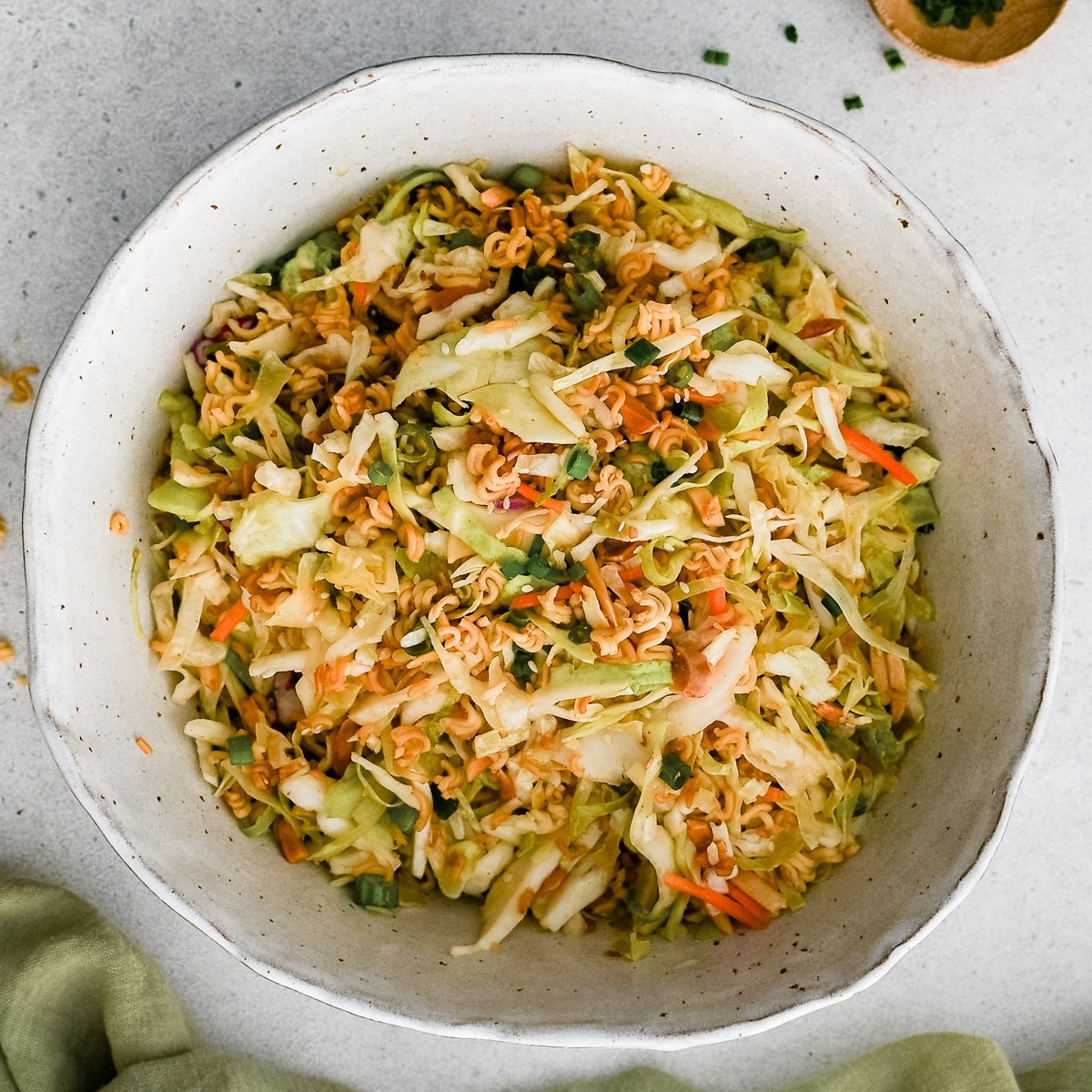 Large mixing bowl filled with a prepared ramen noodle salad consisting of toasted ramen noodles and almonds, coleslaw mix, and sliced green onions tossed in a simple sesame dressing.