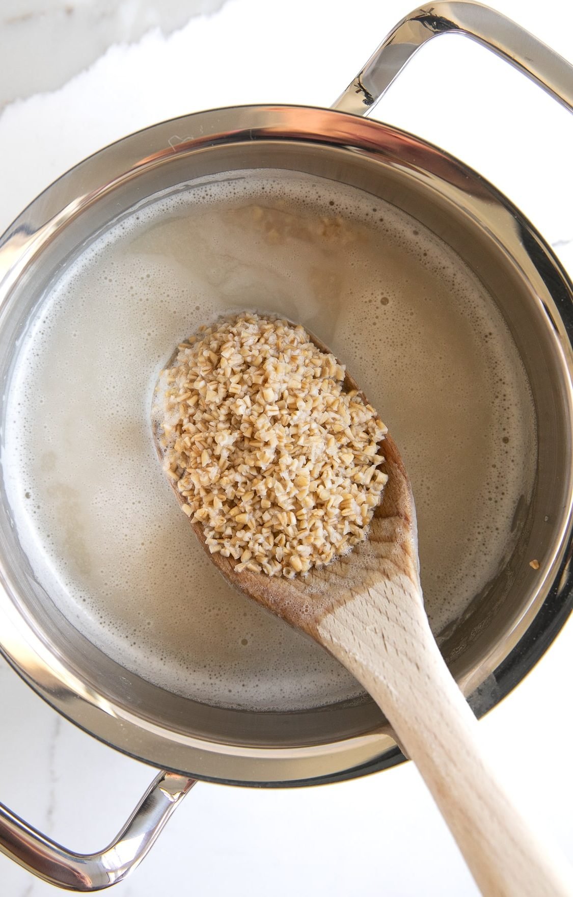 Wooden spoon stirring simmering steel cut oats in a stainless steel pot.