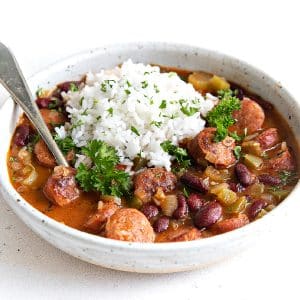 Shallow bowl filled with delicious spicy Cajun red beans and rice topped with cooked white rice and garnished with chopped parsley,