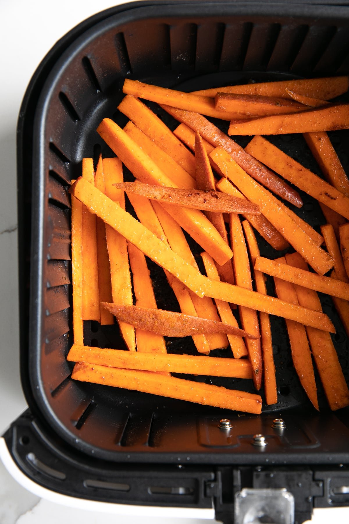 Overhead image looking into the basket of an air fryer filled with uncooked sweet potato fries.