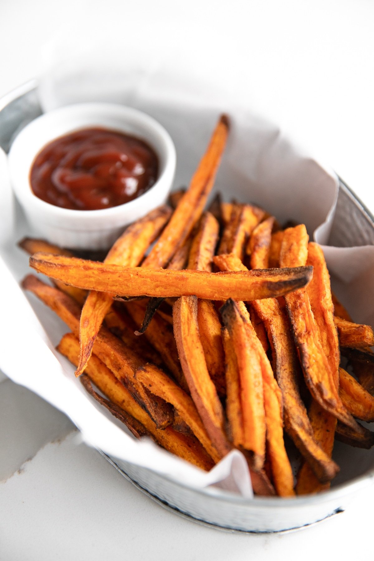 Crispy sweet potato fries made in the air fryer and served in a small metal tin with ketchup.