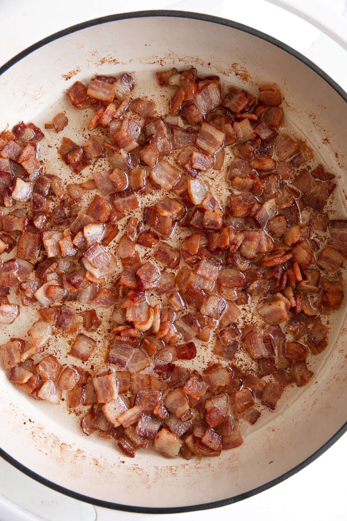 Enameled pan filled with sizzling cooked chopped bacon pieces.