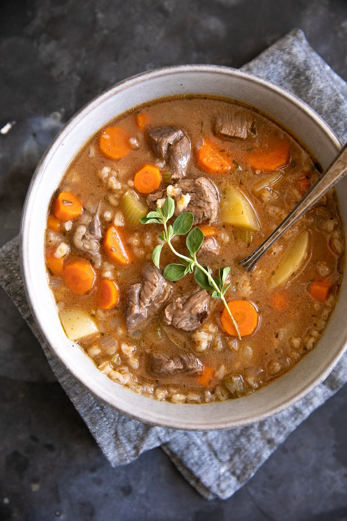 Overhead image of a large soup bowl filled with beef barley soup topped with fresh oregano.