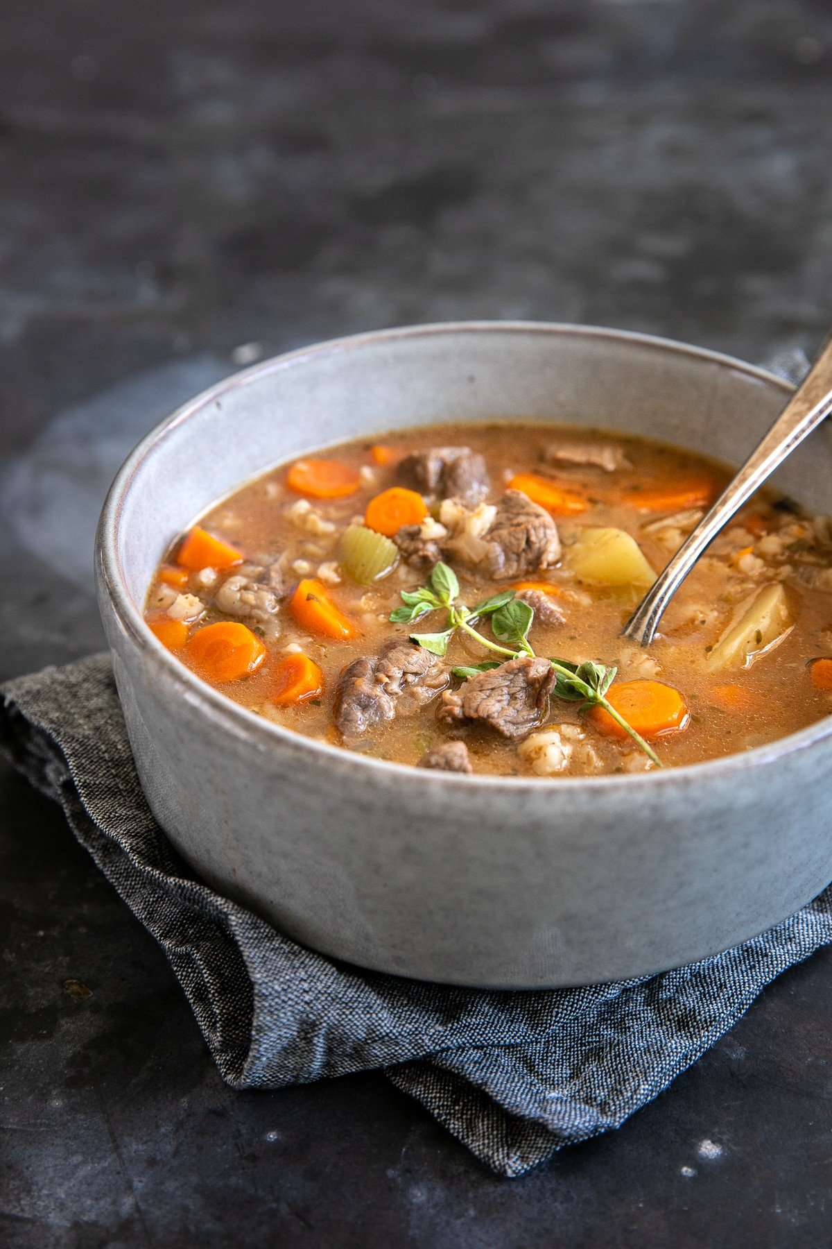 Large bowl filled with beef barley soup made with chunks of beef, carrots, potatoes, and barley in a beef and tomato broth.
