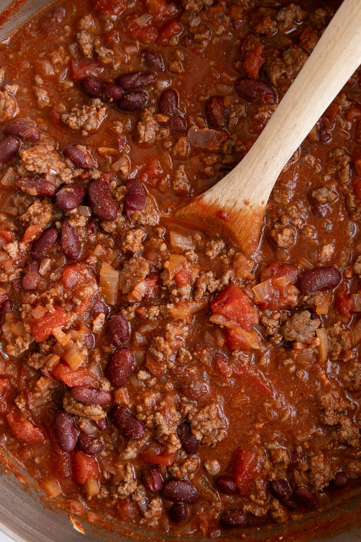 Overhead view of a pot of chili simmering with ground beef, kidney beans, diced tomatoes, and onions in a rich tomato broth.