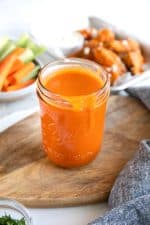Glass mason jar on top of a wood cutting board filled with homemade buffalo wing sauce