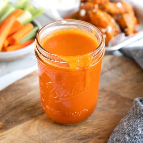 Glass mason jar on top of a wood cutting board filled with homemade buffalo wing sauce