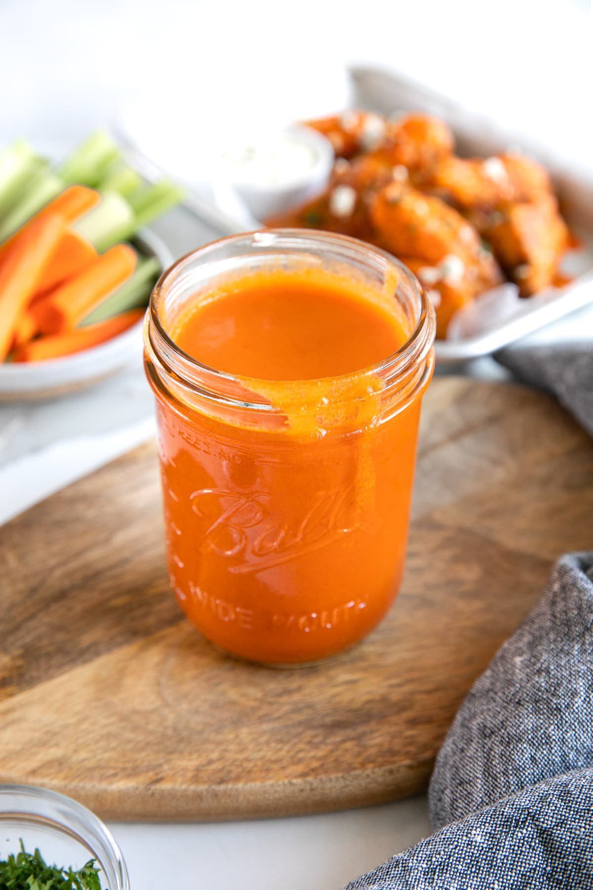 Glass mason jar on top of a wood cutting board filled with homemade buffalo wing sauce.