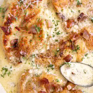 Overhead image of a large skillet filled with seared chicken breast cutlets simmering in a homemade cream sauce with bacon and garnished with parsley.