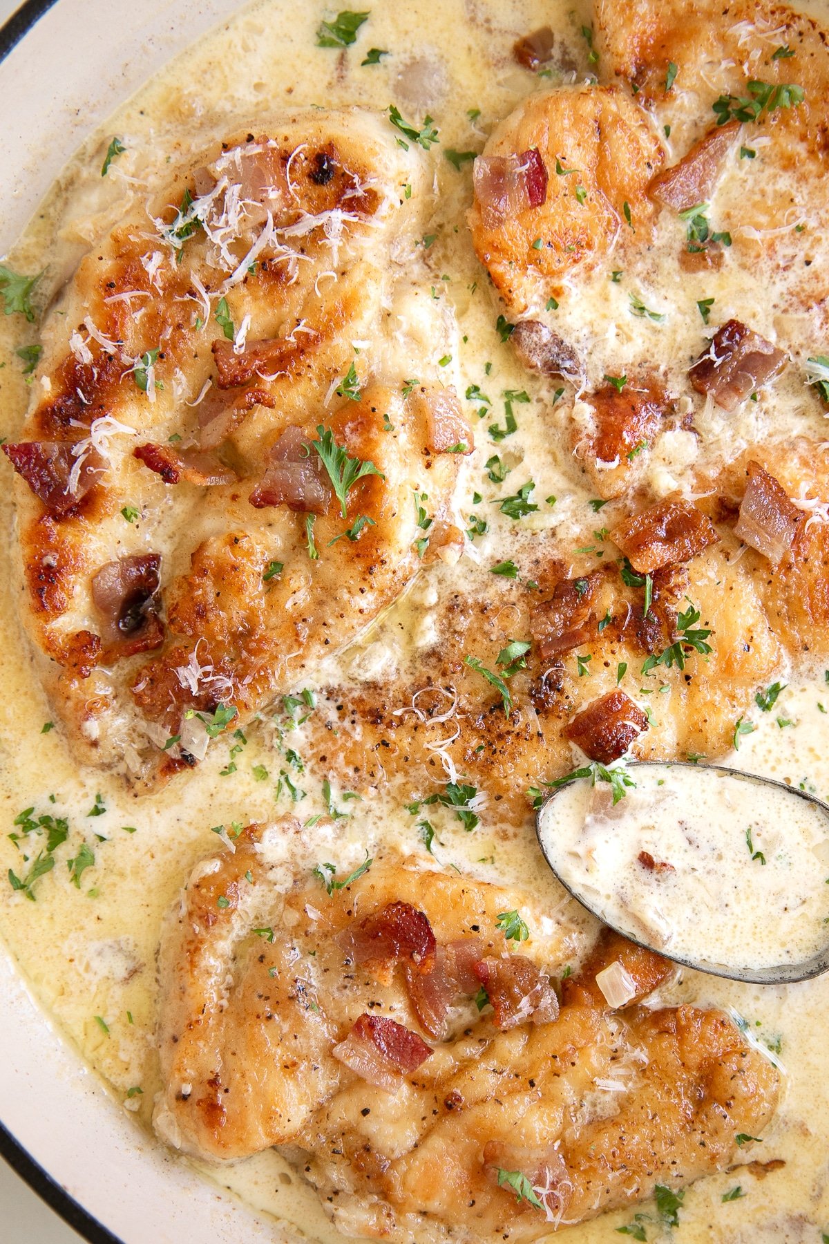 Overhead image of a large skillet filled with seared chicken breast cutlets simmering in a homemade cream sauce with bacon and garnished with parsley.