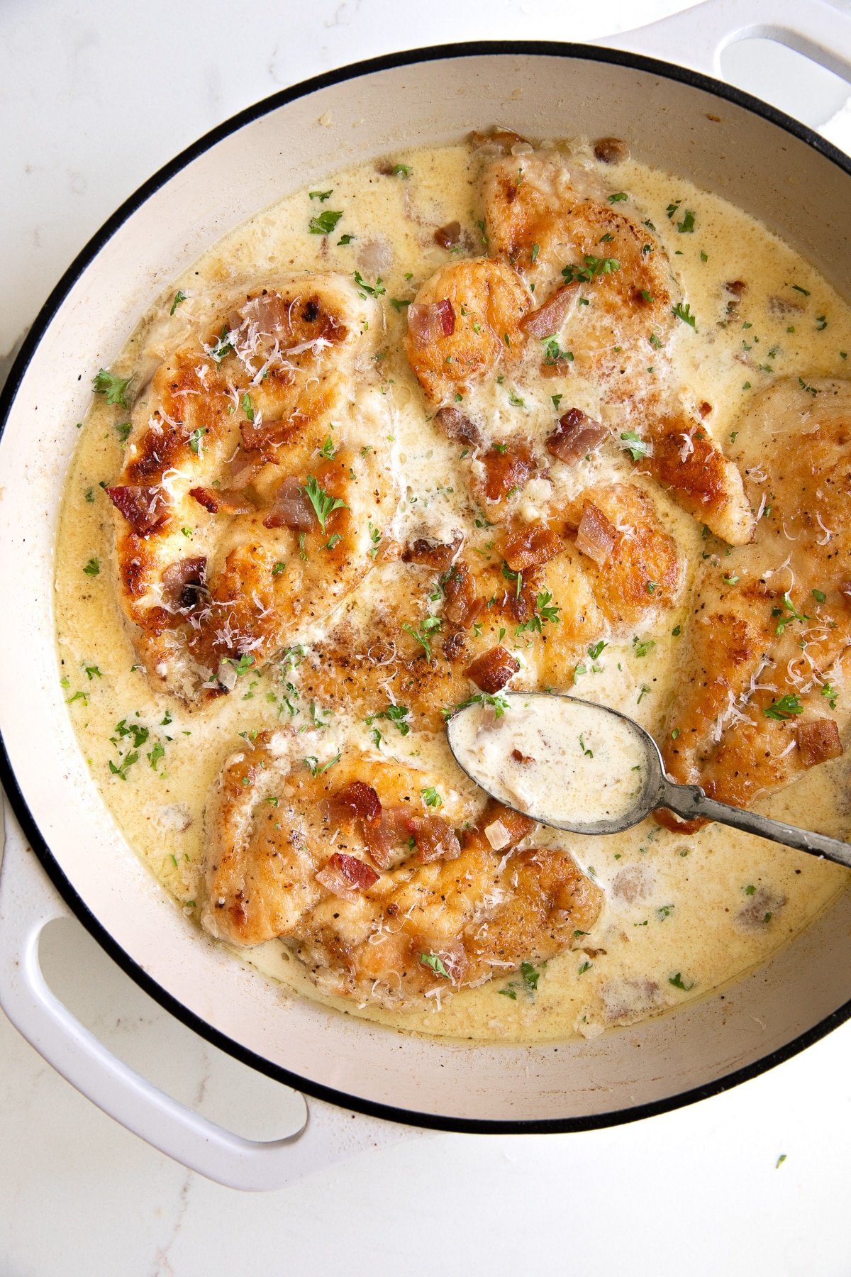 Overhead image of a large skillet filled with seared chicken breast cutlets simmering in a homemade cream sauce with bacon.