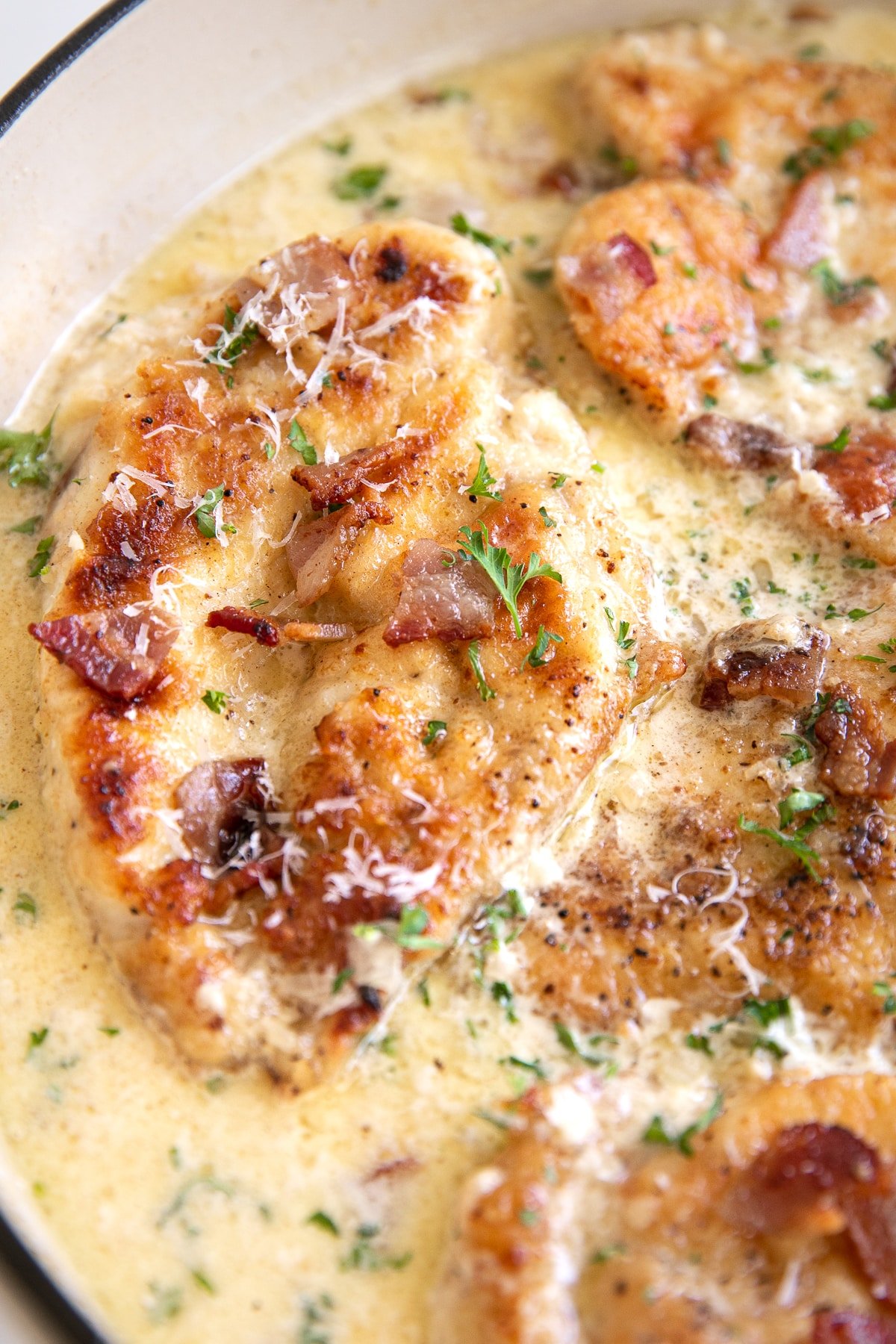 Close up image of a large skillet filled with seared chicken breast cutlets simmering in a homemade cream sauce with bacon.