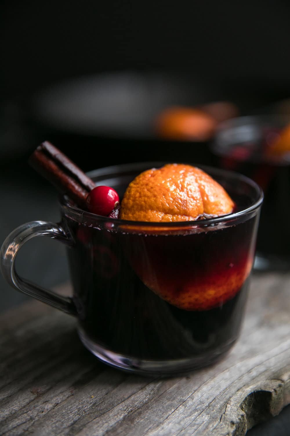 Glass of mulled wine garnished with orange, cinnamon stick, and cranberries.