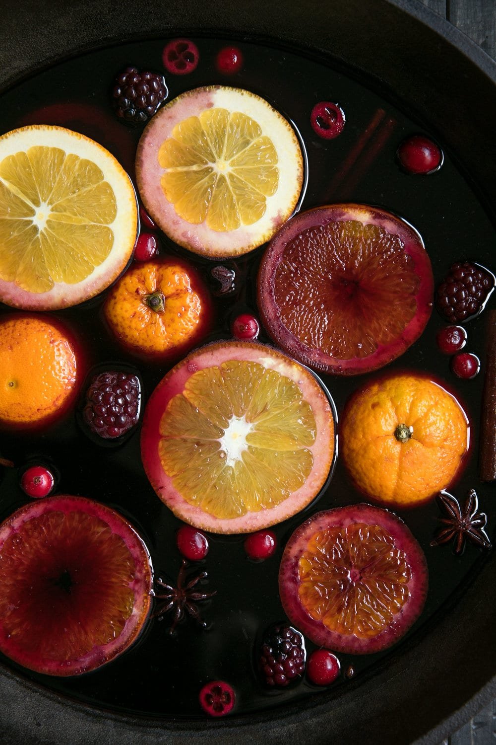 Spiced Mulled Wine in a cast iron skillet with blackberries, cranberries, oranges, cloves, cinnamon sticks, and bourbon.