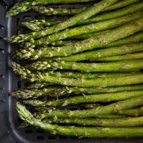 Air Fryer basket filled wit cooked asparagus.