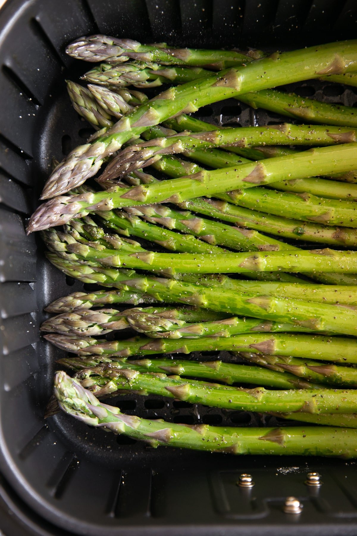 Air fryer basket filled with uncooked asparagus.