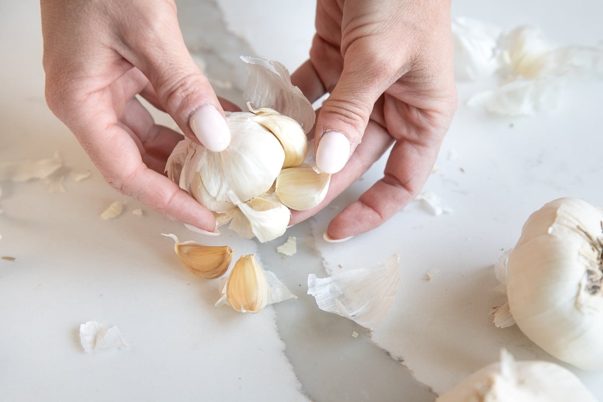 Hands separating the loosened cloves of garlic from the whole bulb.